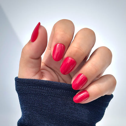 A hand with medium round press-on nails in a rich, glossy cherry red, photographed in natural light with soft shadows — bold, timeless and effortlessly glamorous with a mirror-like gel finish. Also available in an extra short style as Cherry Rouge Petite