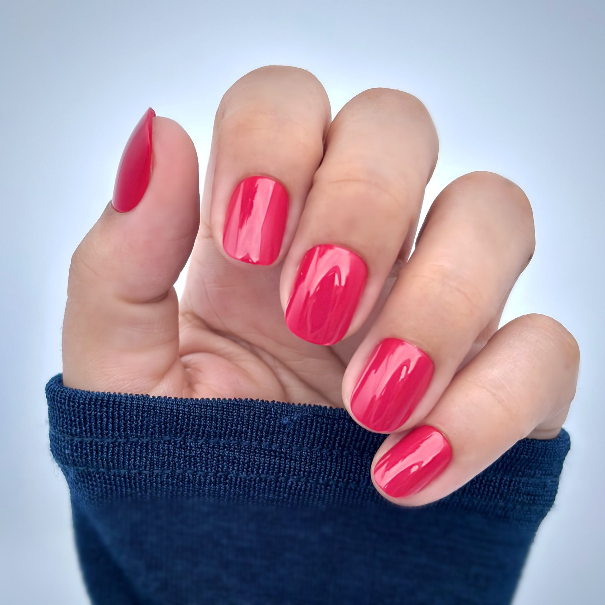 A hand with extra short round press-on nails in a vibrant, high-gloss red, resting against a navy blue sleeve — bold, confident and timelessly elegant