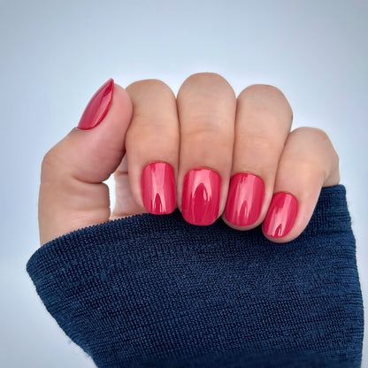 A hand with extra short round press-on nails in a vibrant, high-gloss red, resting against a navy blue sleeve — bold, confident and timelessly elegant