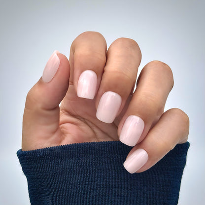 A hand with medium square press-on nails in a soft milky pink, resting gently against a navy blue sleeve — clean, minimal and effortlessly polished